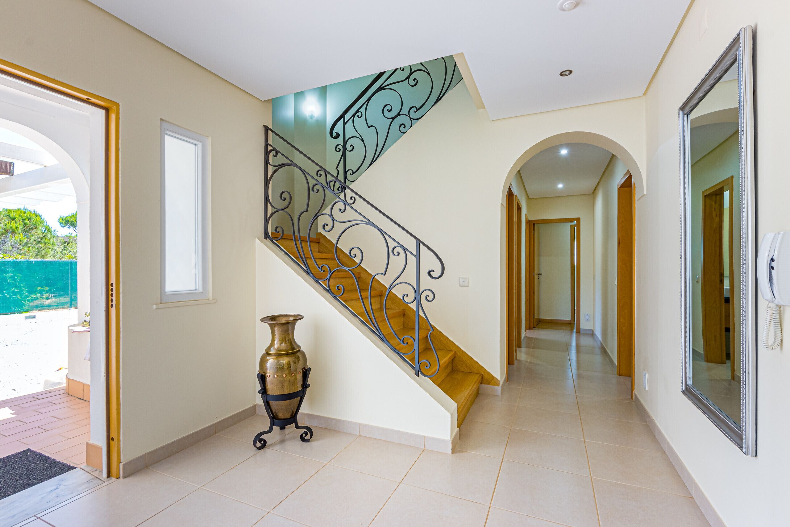 A staircase with ornate metal railings, a wooden handrail, and a vase on the landing.