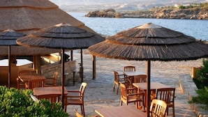 Ein Restaurant am Meer mit reetgedeckten Sonnenschirmen, Holztischen und -stühlen.