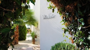Eine weiße Mauer mit der Aufschrift "Villa Foster", umgeben von üppiger Vegetation und Palmen.