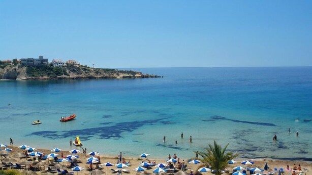 Ein Strand mit klarem, blauem Wasser, Sonnenschirmen und Menschen.
