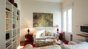 Uma sala de estar com sofá, mesa de centro, estante de livros e uma grande pintura abstrata.