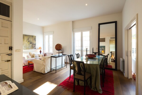 A spacious living area with a dining table, chairs, and a red rug. There is a sofa and a coffee table in the background.