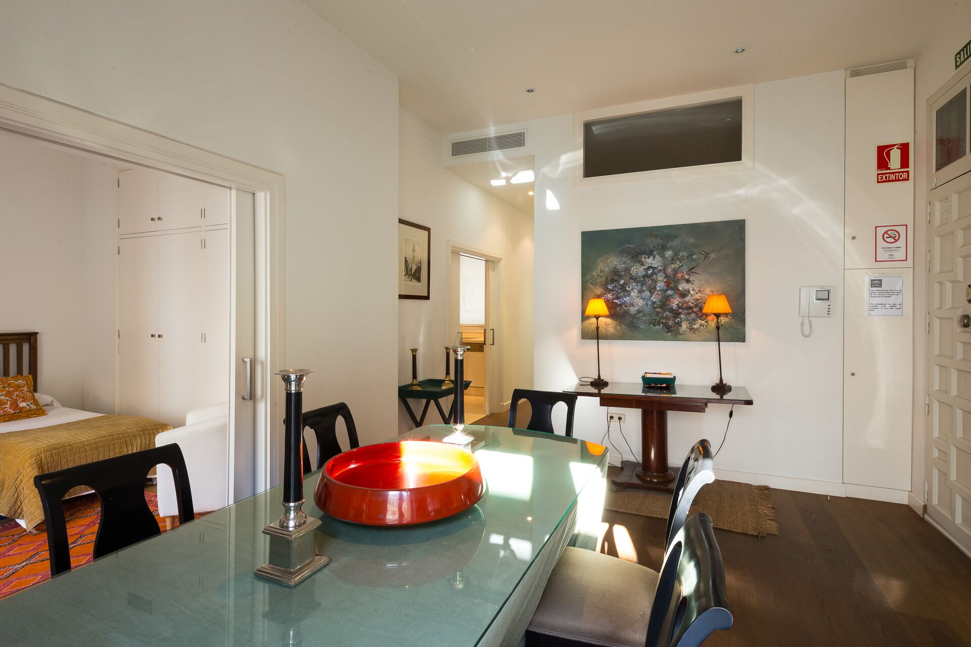 Un coin repas avec une table en verre, des chaises, un bol rouge et deux lampes.