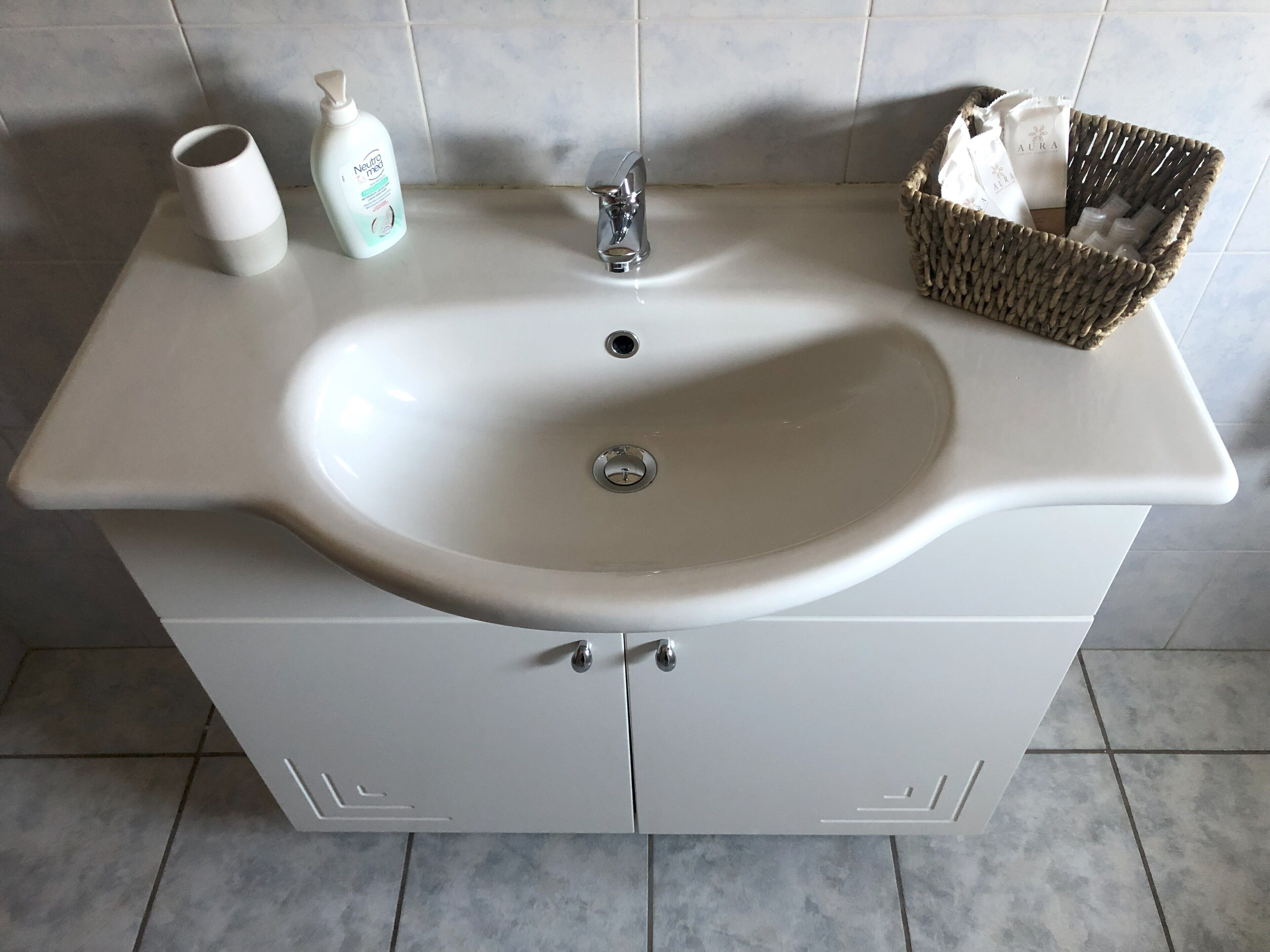 A bathroom sink with a white basin, a faucet, and a bottle of Neutrogena soap. There is a wicker basket with toiletries on the countertop.