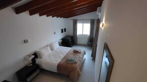 Un dormitorio con cama, mesitas de noche, cómoda, espejo y ventana con cortinas.