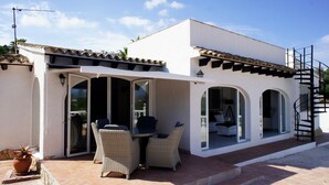 Un edificio blanco con un patio cubierto que incluye mobiliario de mimbre y una mesa.