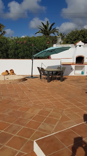 Un espace patio avec une table et des chaises, un sol en briques et un mur blanc agrémenté d’une petite arche.