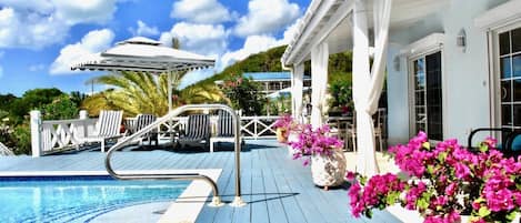 A pool area with lounge chairs, a pergola, and potted flowers.