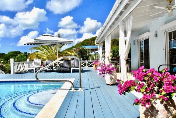 A pool area with lounge chairs, a pergola, and potted flowers.