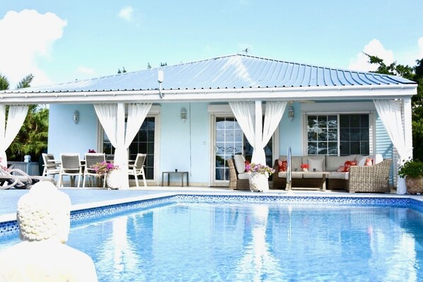 Ein Haus mit Schwimmbad, ausgestattet mit einer überdachten Terrasse, Gartenmöbeln und einem großen Fenster mit Blick auf den Pool.