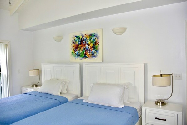 Une chambre d’hôtel avec deux lits, des têtes de lit blanches, une peinture abstraite aux couleurs vives au-dessus des lits et des lampes de chevet.