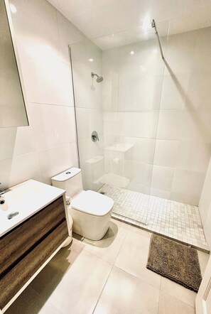 Ein modernes Badezimmer mit einer Duschkabine, einem Holzbadezimmer-Möbel, einer weißen Toilette und einem kleinen Waschbecken.