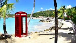 A beach with a red telephone booth, palm trees, and a clear blue sky.