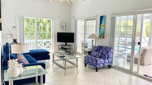 A spacious living room with a large TV, a glass coffee table, and a blue sofa.