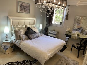 A bedroom with a large bed, a dresser, a vanity, and a chandelier.
