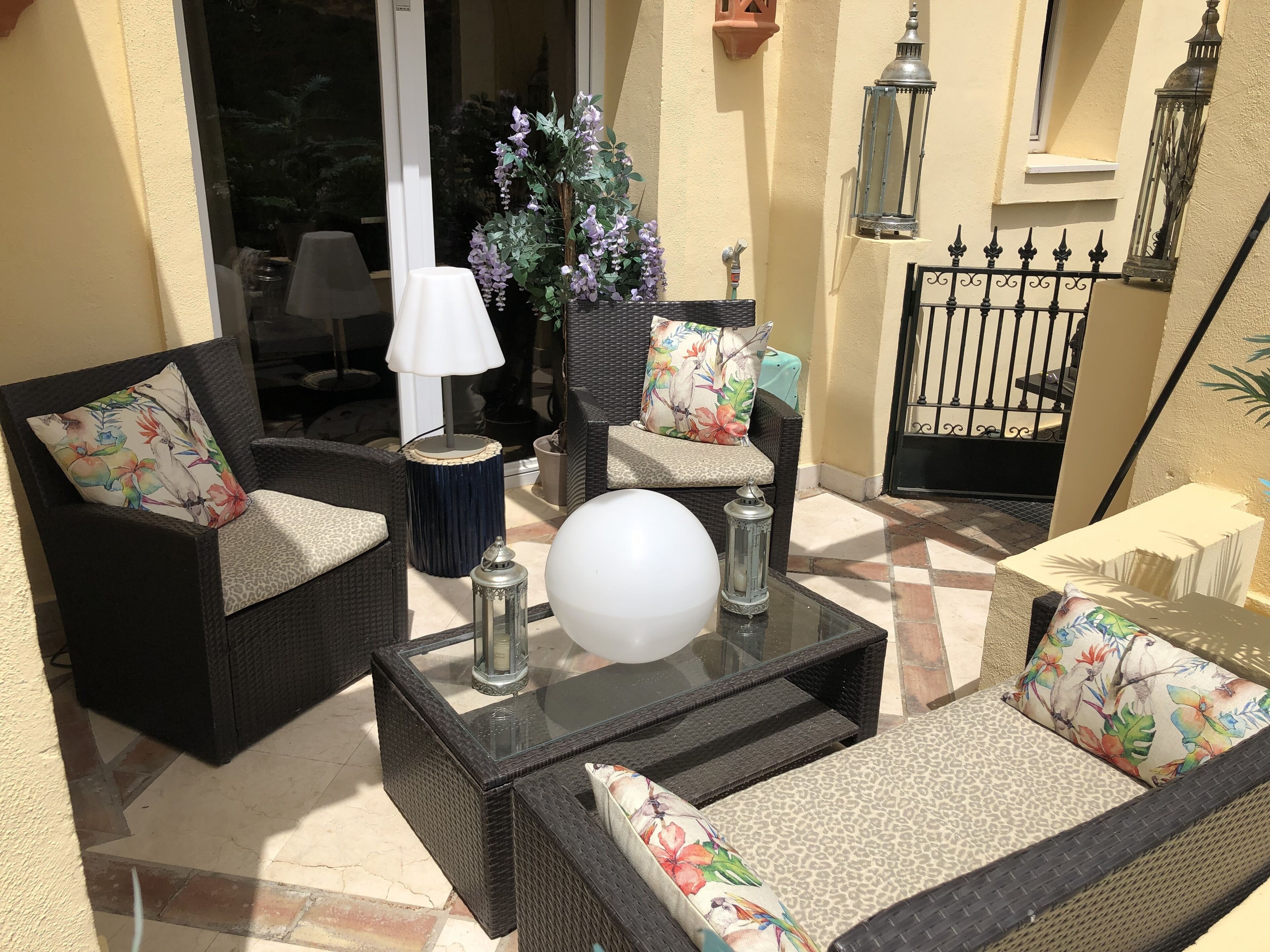 Een zonnig terras met rieten meubels, een glazen salontafel en decoratieve objecten.