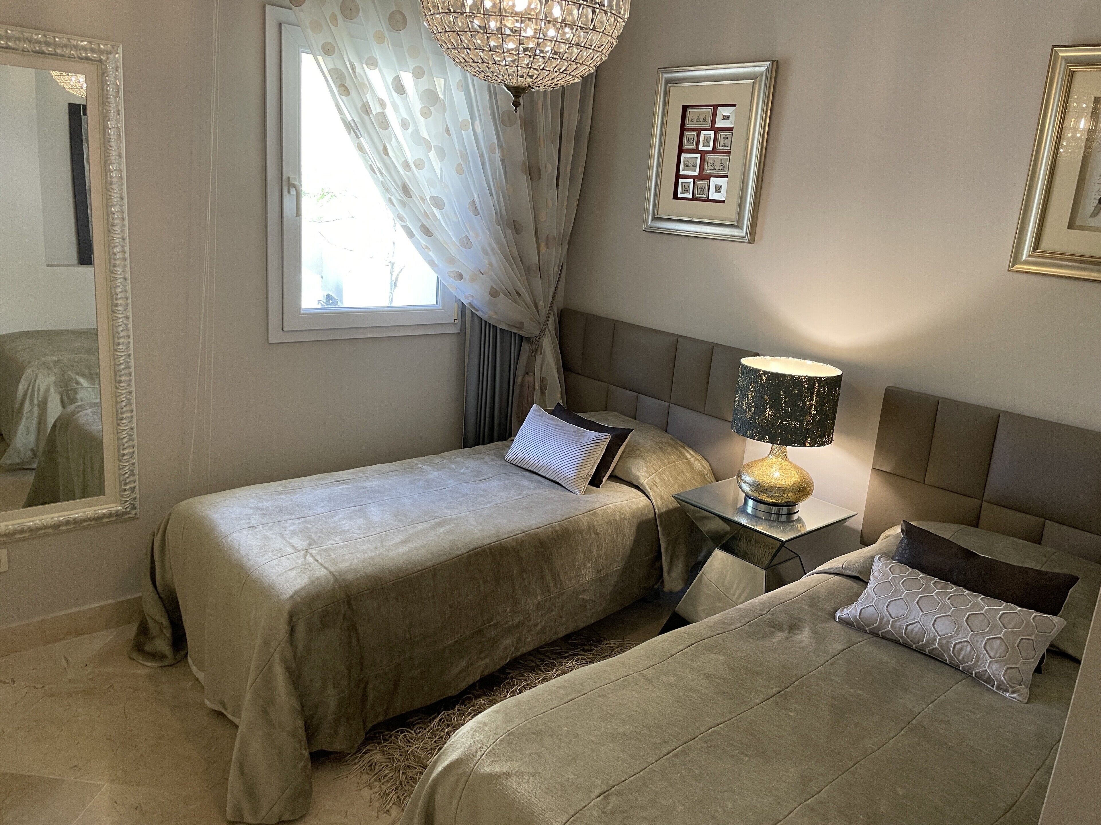 Une chambre avec deux lits, une table de chevet avec une lampe, un miroir et un tableau encadré au mur.