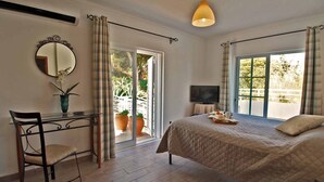 A bedroom with a bed, a desk with a chair, a TV, and a large window with curtains. -  Beautiful 5 bed detached villa, private pool, 700m from the beach - 66875/AL (Castro Marim Praia)