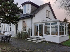 A house with a conservatory, stone patio, and a dining area with outdoor furniture. - Extended Victorian Manor House With Conservatory / large Garden, sleeps 10 (Cardross)