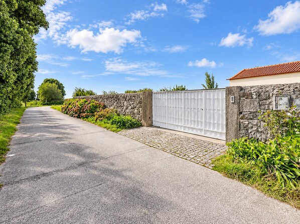A paved driveway leading to a gated entrance with a stone wall and a metal gate.