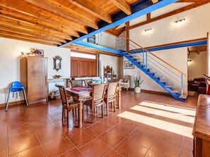 Un vaste espace de vie comprenant une table à manger, des chaises, un escalier bleu et, au fond, une cuisine.