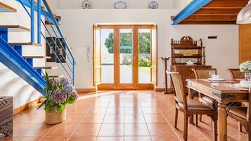 A spacious room with a wooden staircase, a dining area with a table and chairs, and a large sliding glass door leading to an outdoor area.