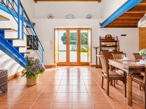 A spacious room with a wooden staircase, a dining area with a table and chairs, and a large sliding glass door leading to an outdoor area.