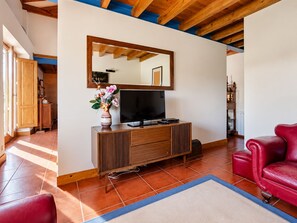 A living room with a television, wooden cabinet, red leather sofa, and a blue rug. - Country House by the Sea (Viana do Castelo)