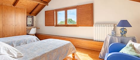 A bedroom with two beds, a window, a radiator, and a table with a lamp.