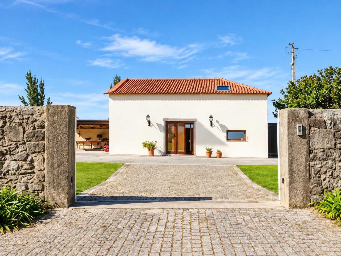 A two-story house with a tiled roof, a stone wall entrance, and a paved driveway.