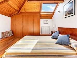 A bedroom with a wooden ceiling, a skylight, a bed with striped bedding, and a framed picture on the wall.