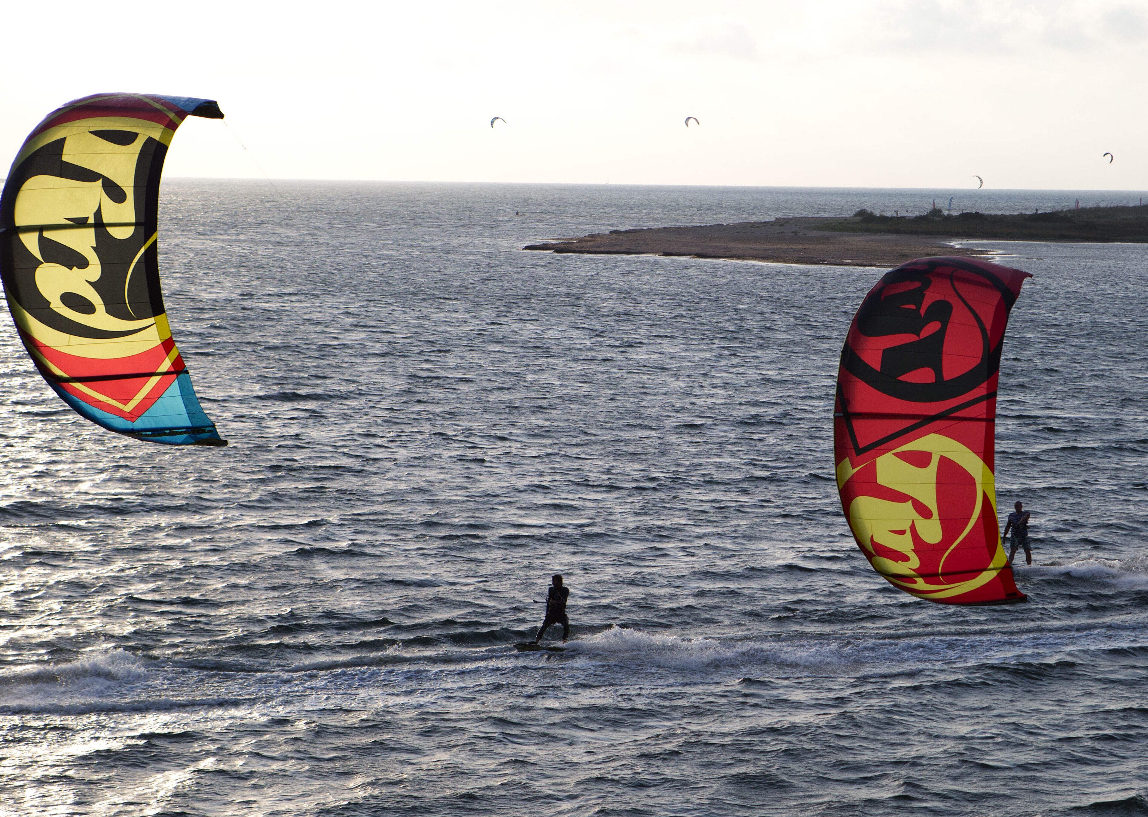 Una playa con dos cometas grandes y una persona practicando surf.