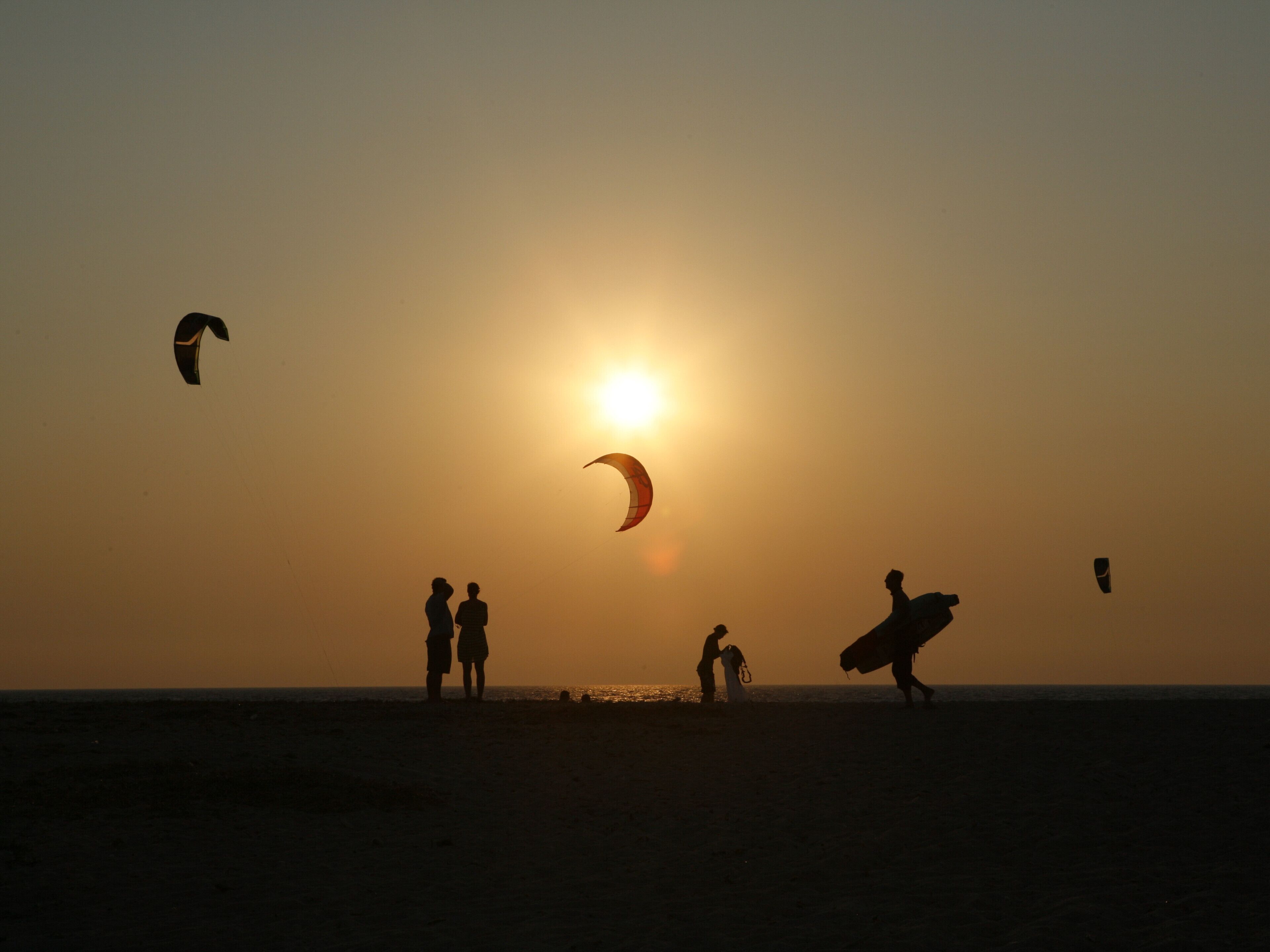 Ein Strandbild mit Menschen und Drachen bei Sonnenuntergang.