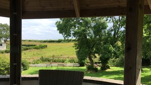 Ein überdachter Außenbereich mit Tisch und Stühlen mit Blick auf eine Wiese und Bäume.
