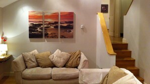 Ein Wohnzimmer mit einem beigefarbenen Sofa, einem Gemälde von einem Sonnenuntergang und einer Treppe.