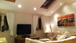 Ein Wohnzimmer mit Flachbildfernseher, einer Couch, einem Fenster mit Vorhängen und einem Oberlicht.