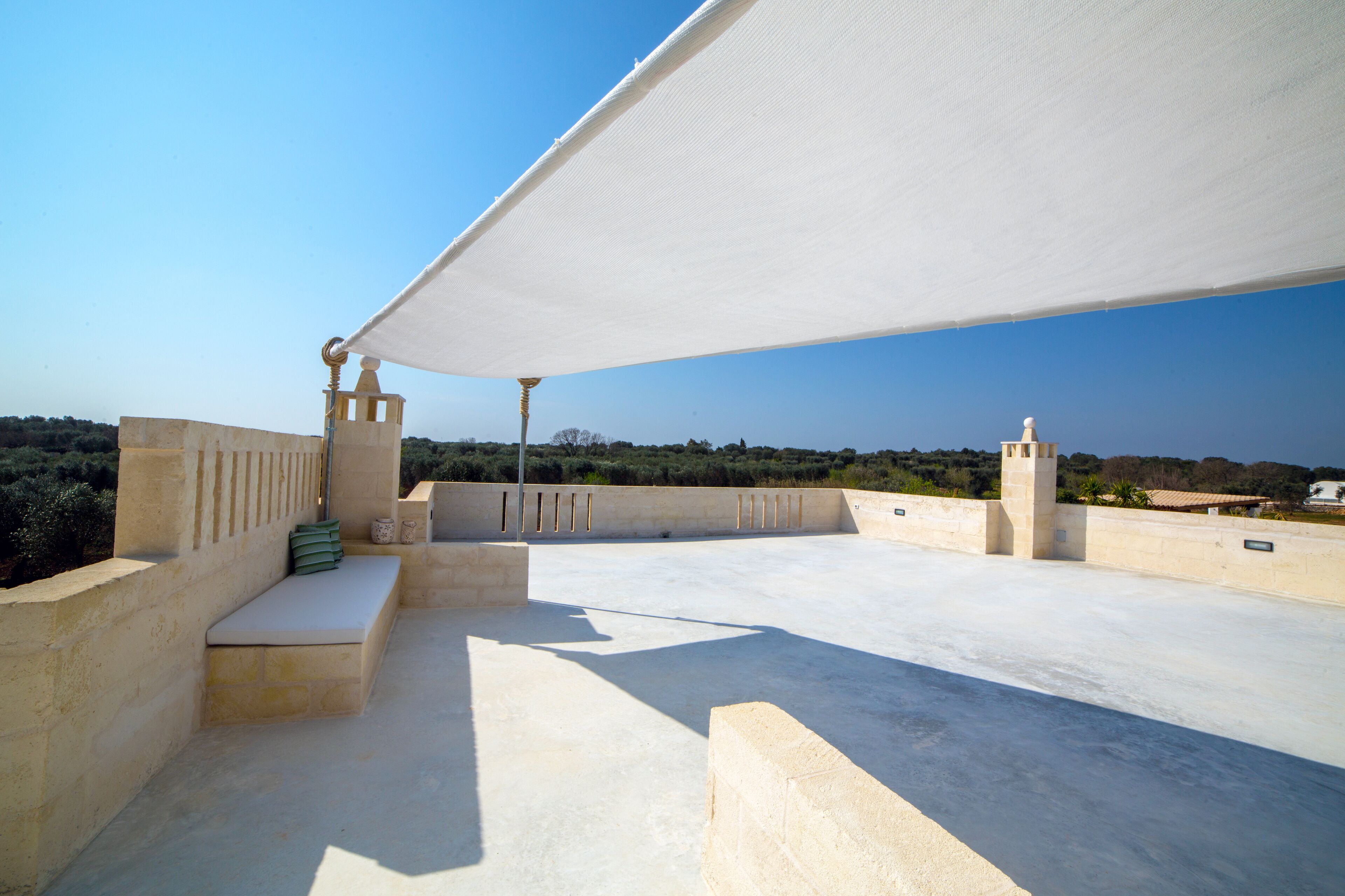 Una terraza al aire libre con toldo blanco, bancos de piedra y vistas al paisaje.