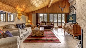 A cozy living room with wooden ceilings, a large window offering a mountain view, a wooden coffee table, and a TV on a wooden cabinet. - Penthouse les Telecabines - La Tzoumaz, 4 Vallees (La Tzoumaz)