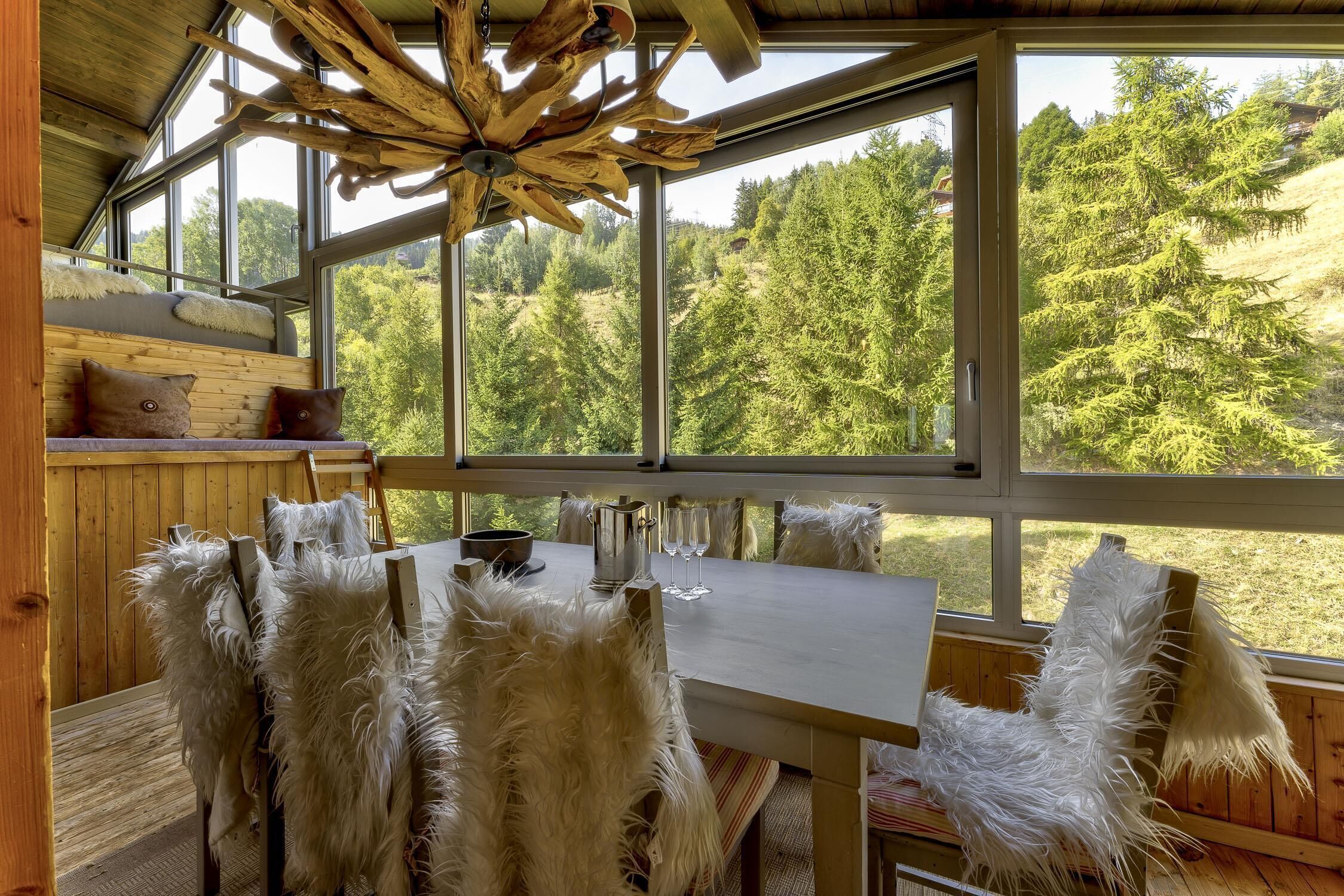 A wooden interior with a large window, a table, and chairs with white fur-like material.
