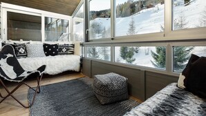 A cozy room with a large window, a sofa with patterned cushions, and a small ottoman. - Penthouse les Telecabines - La Tzoumaz, 4 Vallees (La Tzoumaz)