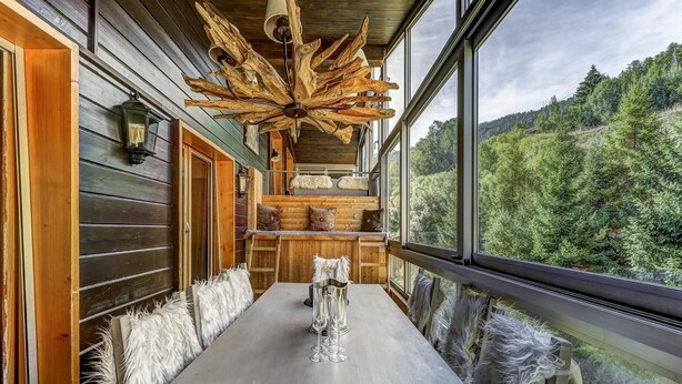 A wooden cabin with a dining area featuring a long table, rustic decor, and a large window offering a view of a forested landscape. - Penthouse les Telecabines - La Tzoumaz, 4 Vallees (La Tzoumaz)