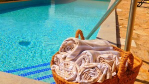 Une piscine à l’eau d’un bleu limpide, un panier en osier rempli de serviettes et un escalier métallique pour accéder à la piscine.