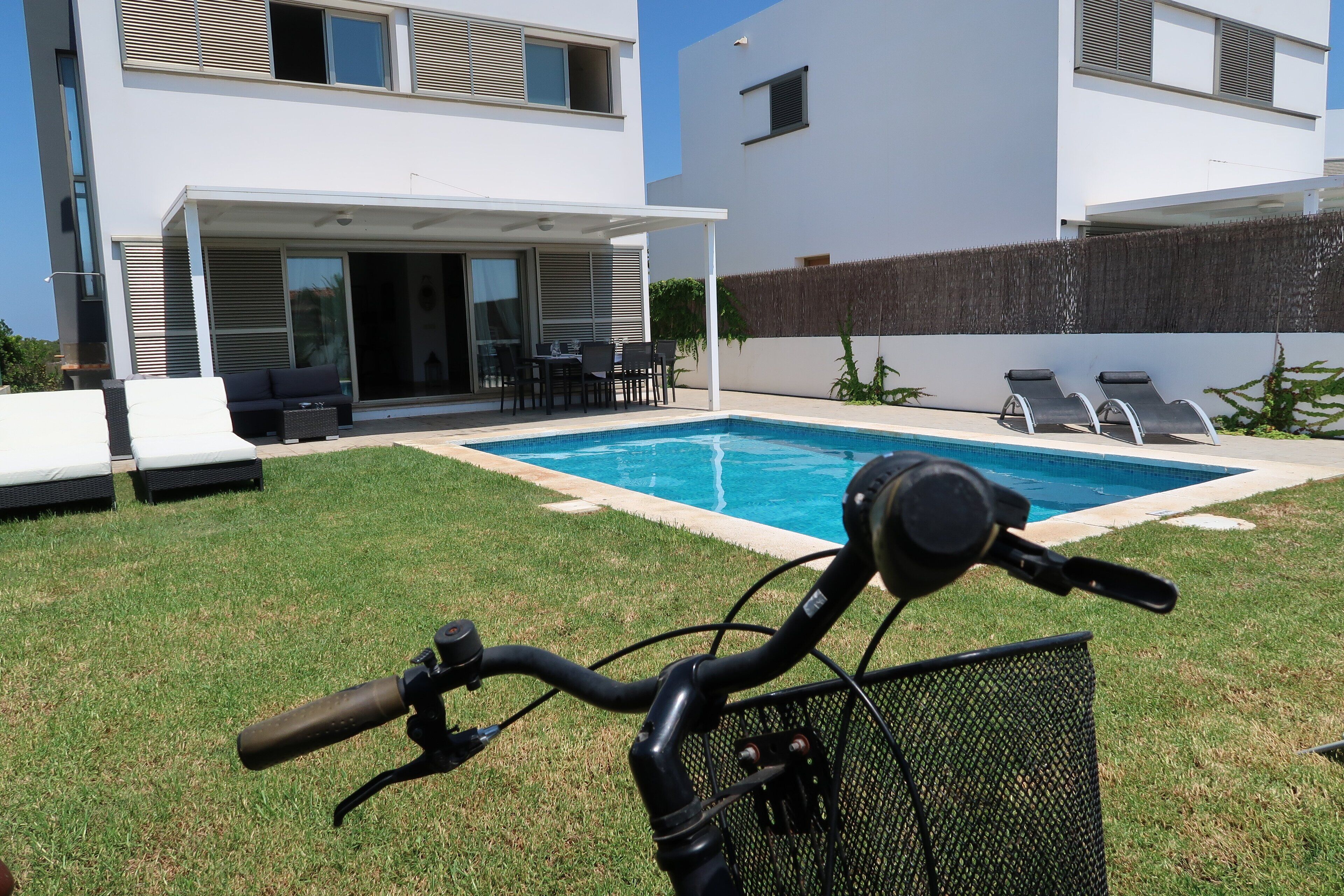 A modern house with a swimming pool, a patio with outdoor furniture, and a bicycle in the foreground.