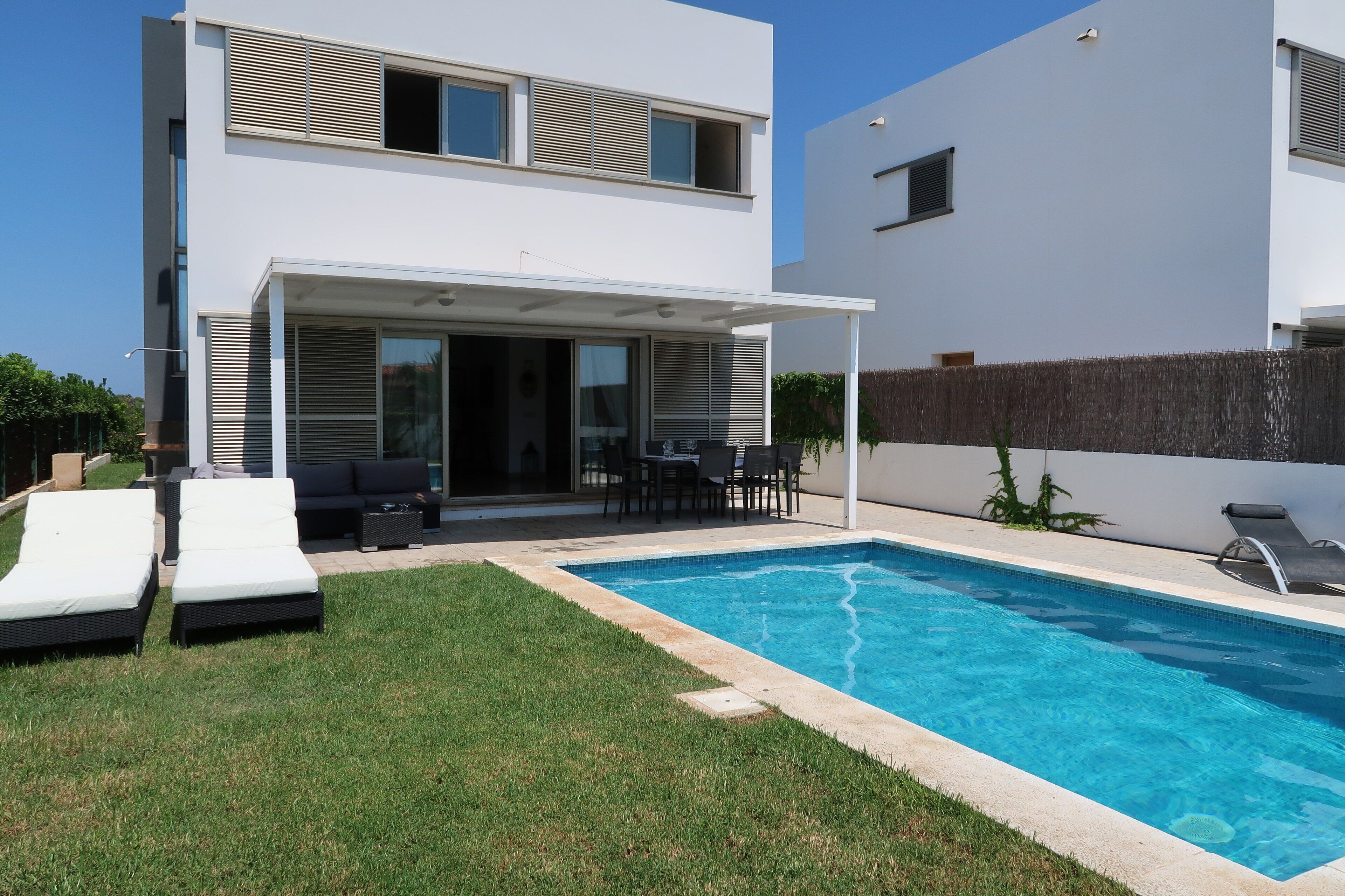 Une maison moderne à deux étages dotée d’une piscine, d’un espace salon extérieur et d’un patio couvert.