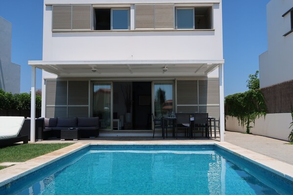 Una casa moderna de dos pisos con piscina, mobiliario exterior y un patio cubierto.