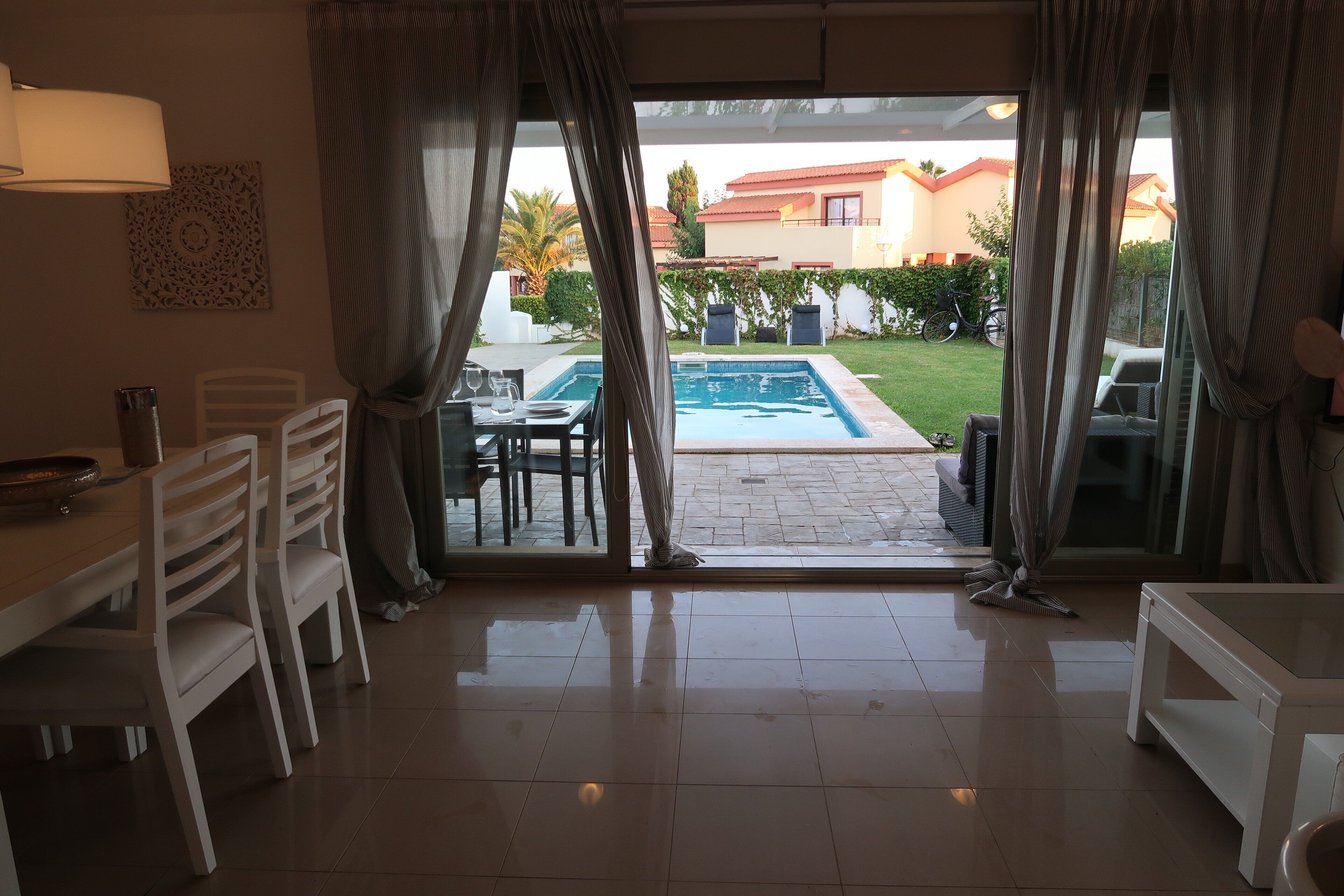 Habitación de hotel con vista a una piscina, zona de comedor con sillas y una mesa, y puerta de vidrio que da al exterior.