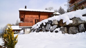 Un chalet in legno con tetto imbiancato dalla neve, un muro in pietra e un balcone.