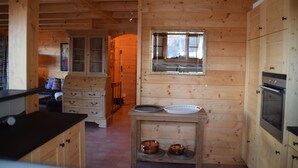 Interno di una baita in legno con angolo cottura, mobili in legno, una finestra e un camino.