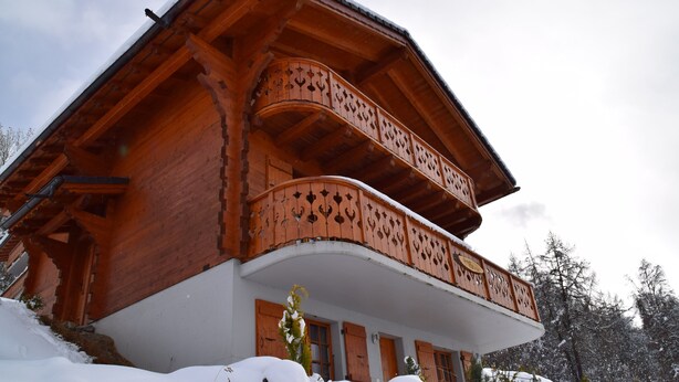 Una baita di legno con un balcone, tetto innevato e parete esterna bianca.