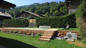 Un patio in legno con una scala che conduce a una panchina, immerso in un giardino curato e circondato da una recinzione di legno.